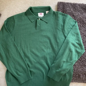 Grön pikétröja från Levi's - Aldrig använd!!!      Säljer en klassisk grön pikétröja från Levi's i storlek L. Tröjan har lång ärm, krage och knäppning framtill med två knappar. Tillverkad i mjukt material och passar perfekt för en stilren look.