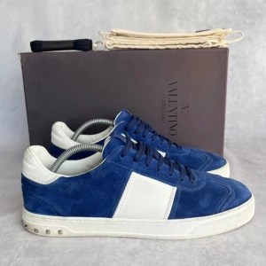 Valentino flycrews - Snygga blå sneakers i mocka från Valentino med vita detaljer och nitar på sulan. Skorna har snörning och en klassisk rund tå. Perfekta för en stilren look, storlek 43