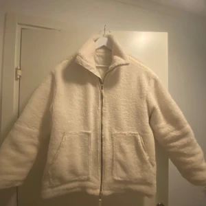 Vit teddyjacka med dragkedja - Mysig vit oversized teddyjacka med dragkedja framtill och två stora fickor. Perfekt för kyliga dagar när du vill hålla dig varm och stilren. Jackan har en hög krage och långa ärmar för extra komfort. Använd ungefär 2 gånger!!💕