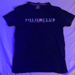 Mörkblå t-shirt från Vinson Polo Club - Säljer en mörkblå Polo T-shirt från Vinson Polo Club med tryck på framsidan. T-shirten har en klassisk rund hals och korta ärmar. Perfekt för en avslappnad stil.