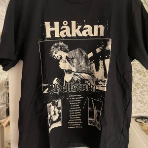 Svart t-shirt med Håkan Hellström-tryck - Säljer en svart t-shirt med ett stort tryck av Håkan Hellström på framsidan. T-shirten har korta ärmar och är perfekt för fans av artisten. Den är gjord i bomull och har en klassisk passform. Kommer från hans turné och har inte sett den någon annan stans. Köpt för 800kr.  Använd 3 gånger och är inte ett fan av artisten därför säljer jag den. 🤗