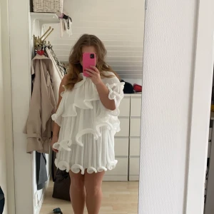 Studentklänning  - Säljer en söt vit kortklänning med volanger. Klänningen har en luftig passform och är ärmlös med en unik design som ger en lekfull look. Perfekt för sommarens alla tillfällen! Hade den till min student och ÄLSKaDE den. 💞PRIS GÅR ATT DISKUTERA VID SNABBAFFÄR💞