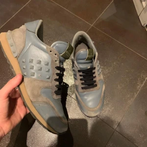 Valentino rockrunner - Snygga sneakers från Valentino i en kombination av grått och blått. Skorna har en unik design med nitar på sidorna och en bekväm sula. Perfekta för en stilren look. De är i okej skick och har bra pris. Dustbag inger.