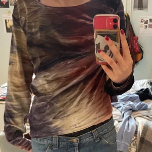 Flerfärgad långärmad topp från Mac Scott - Säljer en unik flerfärgad topp från Mac Scott med ett abstrakt mönster i nyanser av röd, lila och beige. Toppen har långa ärmar och en rund halsringning. Perfekt för dig som vill sticka ut med en färgglad stil. Hör av dig vid intresse!