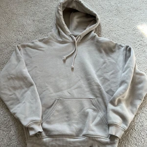 Beige hoodie från Bikbok - Säljer en stilren beige hoodie från Bikbok i storlek XS. Den har en klassisk design med känguruficka och justerbar huva med dragsko. Perfekt för en avslappnad look. Finns några subtila blå fläckar se sista bilden men de syns verkligen knappt