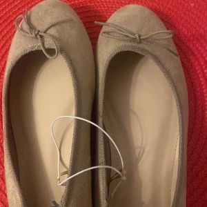 Beige ballerinaskor med rosett - Snygga beige ballerinaskor med en söt rosett på tån. Perfekta för en stilren och bekväm look. Skorna har en mjuk och flexibel sula som ger bra komfort hela dagen.