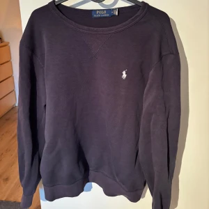 Mörkblå tröja från Ralph Lauren - Säljer en stilren mörkblå tröja från Ralph Lauren med det klassiska logotypbroderiet på bröstet. Tröjan har långa ärmar och en rund halsringning, perfekt för en avslappnad look.