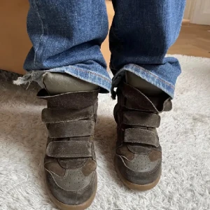 Isabell marant skor  - Snygga bruna sneakers med hög design och kardborreband. Skorna har en kombination av mocka och syntetmaterial, vilket ger dem en unik look. Perfekta för en avslappnad stil.