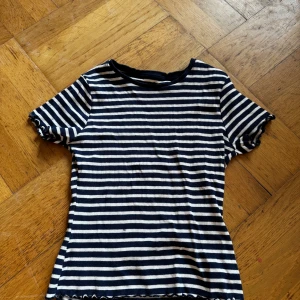Randig topp från Primark storlek 12-13 år - Säljer en jätte in randig topp från Primark i blått och vitt. Toppen har korta ärmar och en ribbad struktur med en söt volangdetalj vid ärmslut och nederkant. Perfekt för sommaren☀️⛱️💕