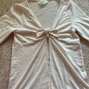 Ljusrosa topp från H&M - Säljer en söt ljusrosa topp från H&M med knytning framtill. Toppen har långa ärmar och en v-ringad design. Perfekt för en avslappnad stil. Hör av dig vid intresse! 🌸