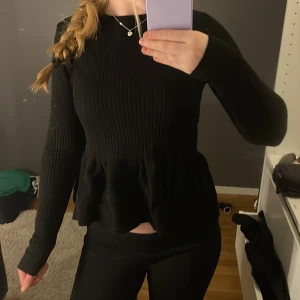 Svart ribbad tröja från Gina Tricot - Säljer en stilren svart ribbad tröja från Gina Tricot. Tröjan har långa ärmar och en volangdetalj vid midjan som ger en fin siluett. Perfekt för att skapa en chic look. Hör av dig vid intresse!