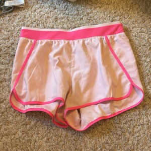 Rosa sport shorts med neonrosa detaljer - Snygga rosa sport shorts med neonrosa kantband och midja. Perfekta för en sportig look eller en avslappnad dag. De har en bekväm passform och är gjorda i ett lätt material.