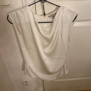 Vit topp - Vit ärmlös topp med en drapering framtill. Perfekt till finare tillfällen.