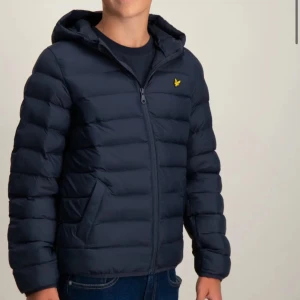 Lyle & Scott Jacka  - Säljer en snygg mörkblå jacka från Lyle & Scott med dragkedja och huva. Jackan har en broderad logga på bröstet och är perfekt för kyligare dagar. Den är långärmad och har en stilren design.