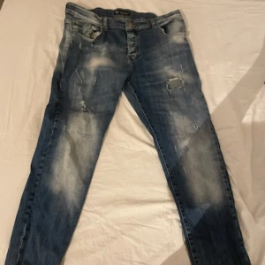 Blå jeans från Philipp Plein - Snygga blå jeans från Philipp Plein med slitna detaljer och en cool tvätt. De har en klassisk femficksdesign och en metalllogga på baksidan. Perfekta för en trendig look. De är i storleken XL och är slum fitt. Äkta och bra sick!