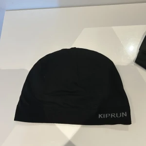 Svart mössa från Kiprun - Säljer en stilren svart mössa från Kiprun. Perfekt för löpning och andra utomhusaktiviteter. Mössan är tillverkad i ett mjukt och bekvämt material som håller dig varm under kyliga dagar. Priset kan sänkas.