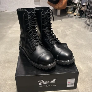 Kängor/combat boots - Säljer extremt fina 14-håls kängor/combat i storlek 43 boots från märker ”Phantom boots” med stålhätta och 100% läder. Köpte dom i början av 2024 på bluefox men har knappt kommit till användning och har putsats och rengjorts efter varje användning. Har haft på extra sulor över originalet så sulorna på kängorna är helt oskadade. Kängorna är som i nytt skick fast pytte lite slitage (höger fots tå, insida fotknöl på båda. Visas på bild). LEVERERAS I ORIGINALLÅDA MED PAPPER (Brandit individual wear)