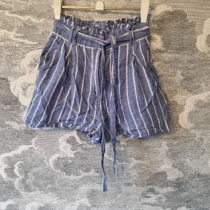 Blå randiga shorts från H&M - Blå och vitrandiga shorts från H&M. De är högmidjade med knytband i midjan och har en avslappnad passform. Shortsen är i mycket bra skick. Jag hittar ingenting att anmärka på.