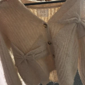 Vit kofta från Zara - Mysig vit kofta från Zara med knappar framtill och dekorativa rosetter. Perfekt för kyliga dagar med sin stickade design och långa ärmar. En stilren och bekväm tröja för alla tillfällen. Storlek 164 men sitter som xs/s🩷