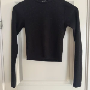 Svart ribbad tröja från Stradivarius  - Säljer en stilren svart ribbad tröja från Stradivarius. Tröjan har en tight passform och långa ärmar, perfekt för en minimalistisk look. Passar bra till både jeans och kjol. Hör av dig vid intresse!
