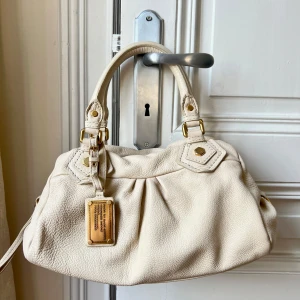 ' - Marc By Marc Jacobs väska. Beige med guldiga detaljer. Väskan är i princip i nyskick då den inte har några defekter! (Se sista bilden för storlek, jag är ca 160). Kan mötas upp i Stockholm eller posta, tryck gärna köp direkt!