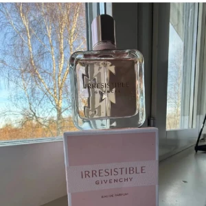 Irresistible Eau de Parfum från Givenchy - Säljer en elegant flaska av Irresistible Eau de Parfum från Givenchy. Parfymen kommer i en stilren, fyrkantig glasflaska med en rosa ton och ett matchande lock. Förpackningen är ljusrosa med Givenchy-logotypen i silver. Perfekt för den som älskar lyxiga dofter.
