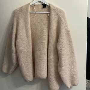 Beige stickad kofta från Lindex - Mysig beige stickad kofta från Lindex. Perfekt för kyliga dagar med sin mjuka och bekväma passform. Koftan har långa ärmar och en öppen design utan knappar. Ett måste för garderoben!