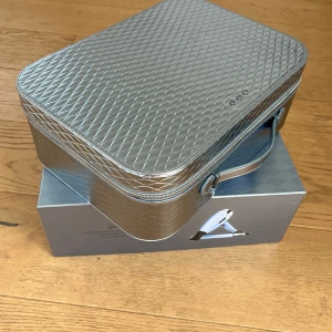 Silverfärgad väska från ghd - Snygg silverfärgad väska från ghd med quiltad design. Perfekt för att förvara stylingverktyg eller andra tillbehör. Väskan har ett praktiskt handtag och dragkedja för enkel användning.