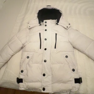 Vit Explorer Puff jacka med huva - Säljer en snygg vit pufferjacka med huva och svarta detaljer. Jackan har dragkedja och knappar framtill samt praktiska fickor. Perfekt för kalla dagar!