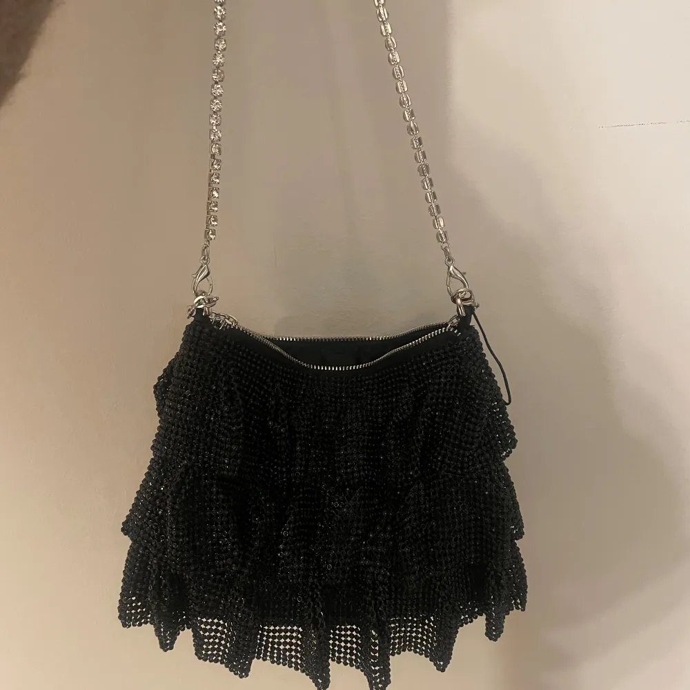 Snygg svart axelväska med glittriga detaljer och volang. Man kan både ha den kort över axeln eller som på min 3dje bild. Den är från Zara och köptes för ca 1,5 år sedan men är aldrig använd🥰. Laukut & Käsilaukut.