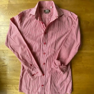 Rutig röd skjorta från Ströms - Snygg röd och vit rutig skjorta från Ströms i slim fit-modell. Skjortan har klassisk krage, långa ärmar och röda knappar framtill. Tillverkad i mjuk bomull som känns skön mot huden. Perfekt för dig som gillar stilrena detaljer och mönster.