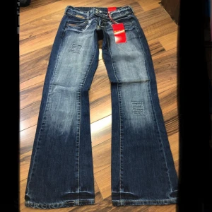 Blå bootcut jeans från Glago - Snygga blå jeans från Glago med bootcut passform och slitna detaljer vid fickor och lår. Jeansen har dubbla knappar i midjan, ljusare tvättade partier och dekorativa sömmar. Perfekt för dig som gillar en cool och avslappnad stil. 