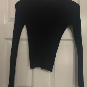 Svart ribbad långärmad tröja - Säljer en svart långärmad tröja med ribbad struktur och tight passform. Tröjan har en enkel, klassisk design med rund hals och är perfekt för layering. Materialet är stretchigt och sitter snyggt mot kroppen.