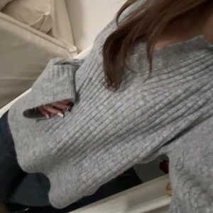 Grå ribbad stickad tröja med krage - Mysig grå stickad tröja med ribbad struktur och bred krage som går ner i en v-ringning. Tröjan har lång ärm och är lite loose i passformen, perfekt att slänga på sig när det är kyligt ute. Materialet känns mjukt och värmande, passar till jeans eller leggings.