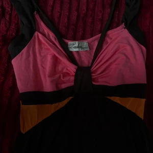 Färgglad långklänning från Toda Woman - Snygg långklänning med breda axelband och omlott-detalj framtill. Klänningen har färgblock i rosa, svart och orange, vilket ger en cool vibe. Materialet känns mjukt och lätt, perfekt för varma dagar. Passformen är normal och klänningen har en flowy siluett.💖💖💖