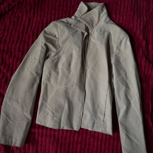 Beige mockajacka från iSoLina - Snygg beige mockajacka från iSoLina med cool ståkrage och dragkedja framtill. Insidan är fodrad med glansigt satinmaterial som känns lyxigt mot huden. Jackan har en clean och stilren look som passar till många outfits.🐆🐆💖 finns tecken på använding. 