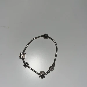 Silverfärgat armband med berlocker - Snyggt armband i silverfärg med flera unika berlocker, bland annat en med bokstaven A och detaljerade former. Kedjan är tunn och smidig, perfekt för att ge din stil en personlig touch. Passar dig som gillar att sticka ut med accessoarer, funkar till både män och kvinnor!