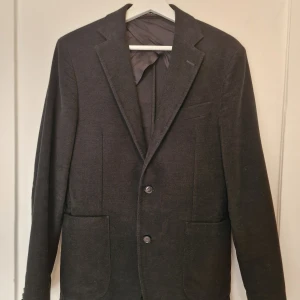 Svart kavaj från Oscar Jacobson - Stilren svart kavaj från Oscar Jacobson. Materialet känns mjukt och har en matt finish, perfekt för dig som gillar tidlös design. Ytterst sparsamt använd, nästan som ny och kostade närmare 4000 kr. 