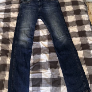 Blå Hugo Boss jeans slim fit - Snygga mörkblå jeans från Hugo Boss med klassisk femficksdesign och diskreta slitningar framtill. Modellen har raka ben och normal passform, perfekt för dig som gillar stilrena och tidlösa jeans. Materialet är 98 % bomull och 2 % elastan med Boss-logga på fickan.