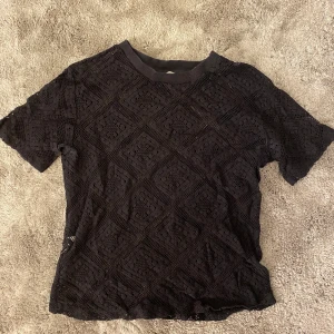 Svart spetsblus från MNG XS - Säljer en svart blus från mango i storlek XS. Blusen är helspets med geometriskt mönster och är genombruten, vilket ger en snygg och luftig känsla. Den har korta ärmar och ribbad kant vid halsen. Perfekt att styla lager på lager.