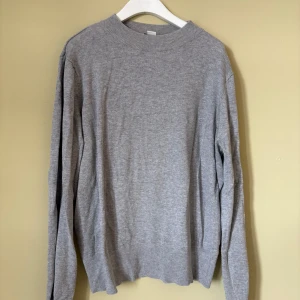 Grå långärmad tröja från Monki - En enkel och stilren grå tröja från Monki i storlek M. Tröjan har rund hals, långa ärmar och är tillverkad av en mjuk blandning av viskos och polyamid. Perfekt för dig som gillar minimalistisk look och vill ha något bekvämt till garderoben.