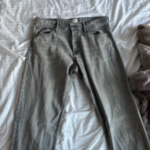 Grå loose fit jeans från Jack & Jones - Säljer ett par grå jeans från Jack & Jones, modell Loose/Chris. De har loose fit och klassisk femficksdesign med silverfärgade nitar. Jeansen är raka i benen och har en snygg, ljusgrå tvätt. Perfekt för dig som gillar avslappnad stil.
