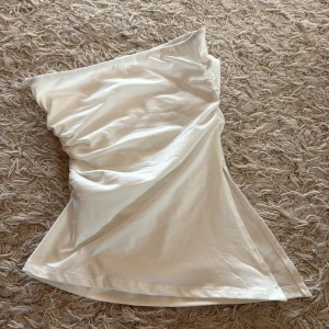 Vit bandeau tubtopp - Säljer en vit bandeau tubtopp med enkel och clean design. Toppen är ärmlös och har en mjuk, stretchig passform som sitter snyggt över överkroppen. Perfekt för dig som gillar minimalistisk stil och vill ha en topp som funkar till många olika looks. Slits vid sidan, älskar! Endast provad.