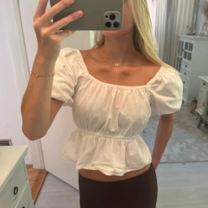 Vit croppad blus med puffärm - Superfin vit blus med croppad passform och puffiga korta ärmar. Toppen har en söt volang nedtill och en bred, fyrkantig urringning som ger en romantisk vibe. Tillverkad i mjuk bomull, perfekt för varma dagar och snygg att styla med höga jeans eller kjol.