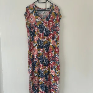 Blommig klänning från Esmara - Säljer en färgglad klänning från Esmara med blommigt mönster i rött, rosa, blått och gult. Klänningen har v-ringning, ärmlös design och mjukt material som känns skönt mot huden. Nyskick, bara använd en gång. 