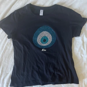 Evil Eye Svart t-shirt med blått tryck Kos - Svart t-shirt från Regent med rund hals och korta ärmar. Aldrig använt som ny - Storlek M men är liten i storlek som XS/S