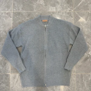 Grå ribbad kofta med dragkedja - Säljer en stilren grå kofta från Ralph Lauren med ribbad struktur och hel dragkedja framtill. Perfekt för dig som gillar enkel och clean look. Långärmad modell med rund hals och mjukt material som känns skönt mot huden.