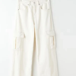 Vita wide cargopants med fickor low waist - Säljer ett par vita cargopants med breda ben och stora fickor på sidorna. Byxorna har en loose passform och är tillverkade i bomull, vilket gör dem både sköna och snygga. Perfekta för dig som gillar streetstyle och vill ha plats för allt i fickorna. Low waist