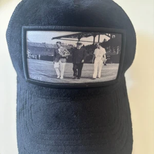 Svart keps WON X FORTE med fototryck - Cool svart keps från WON X FORTE med mesh baktill och ett unikt svartvitt fototryck framtill. Kepsen har böjd skärm och klassisk trucker-modell. Perfekt för dig som vill sticka ut med en stilren accessoar.