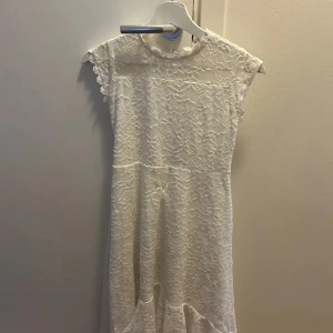 Vit spetsklänning med öppen rygg - Säljer en vit långklänning med spetsdetaljer och vacker öppen rygg. Klänningen har korta ärmar med söt kant och ett romantiskt spetsmönster över hela plagget. Perfekt för dig som vill ha en elegant och feminin look med extra detaljer.